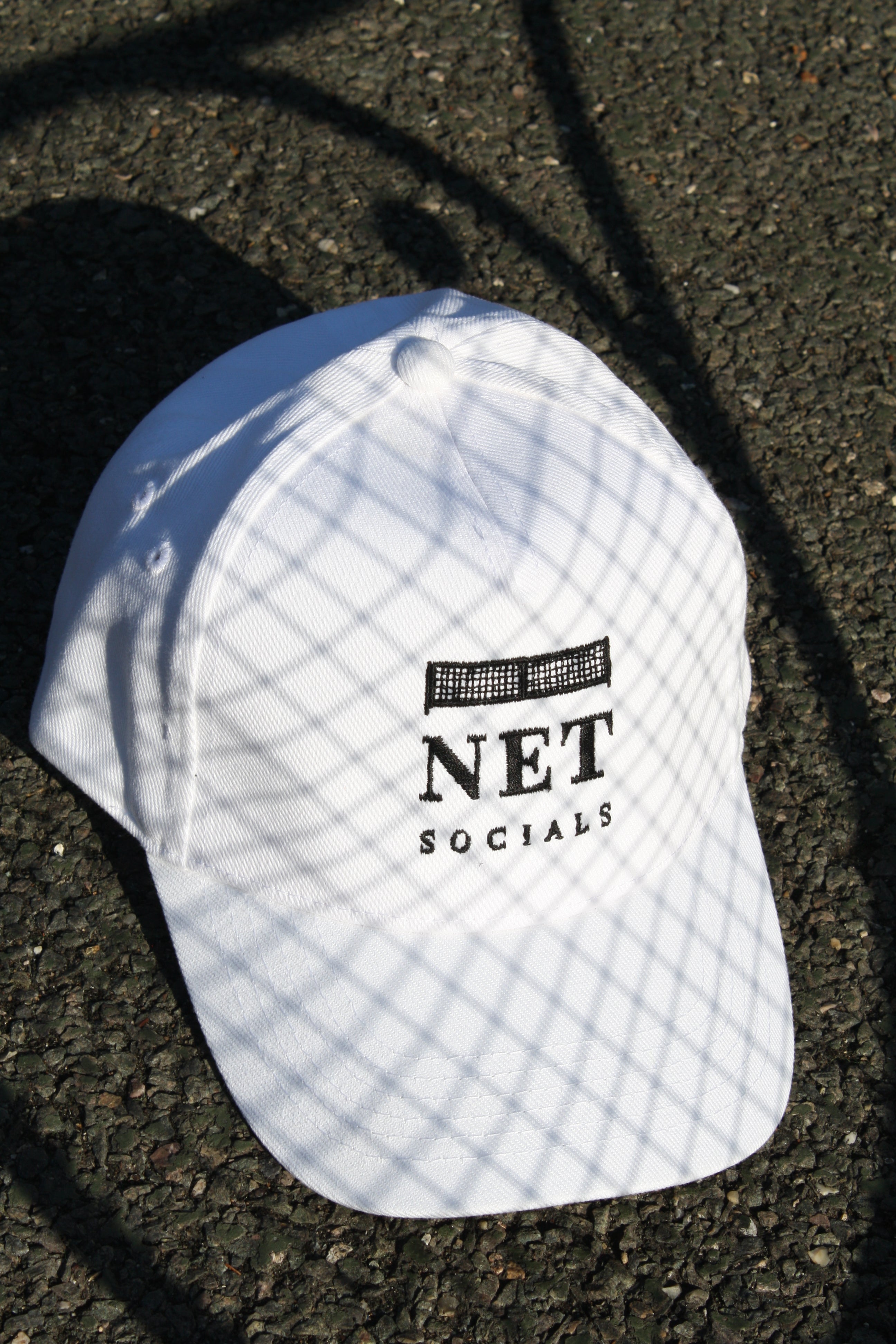 White cap with 'NET SOCIALS' logo on a dark surface