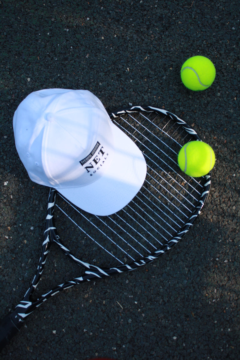 Tennis racket and balls on a dark surface with Net Collective cap